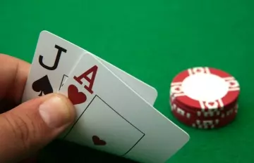 a pure blackjack with a jack and ace being held against a poker table background with a pile of chips