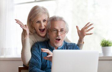 middle aged couple happy from winning playing online slots on their laptop