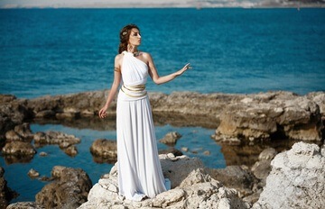 brown-haired women in front of the sea dressed as goddess Athena in a white dress