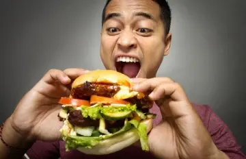 man anxiously eating a double burger with all the fixings