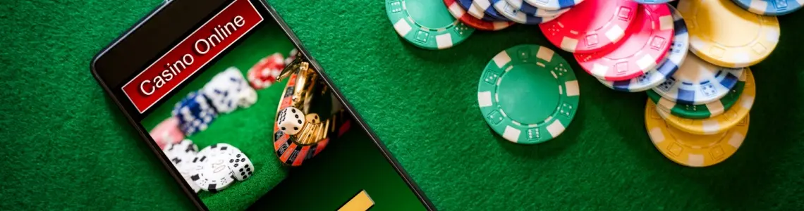 a smartphone on a green felt tabletop with Casino Online on the screen and many casino chips next to the phone