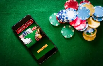 a smartphone on a green felt tabletop with Casino Online on the screen and many casino chips next to the phone