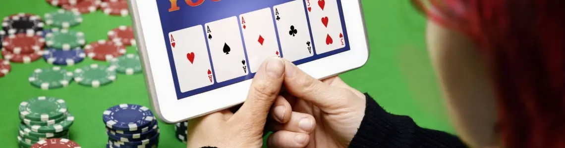 a red-haired woman holding a tablet with an online casino on the screen showing four aces in a video poker hand.