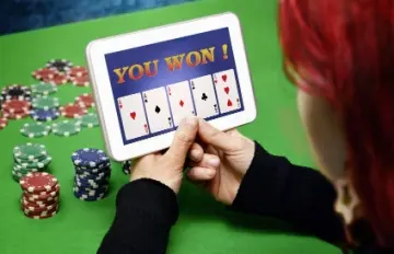 a red-haired woman holding a tablet with an online casino on the screen showing four aces in a video poker hand.