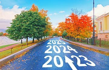 an open road with fall leaves on one side and a green leafed tree on the other side heading into 2023, 2024, and 2025