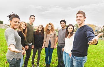 a group of young people in the countryside welcoming a new person to their friendly group