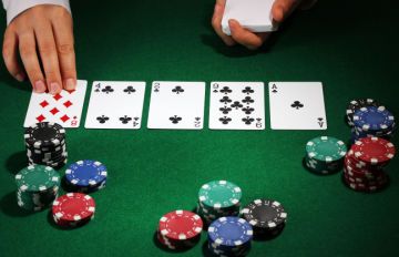 the dealer placing the river card in a game of Texas Holdem.  The green felt table has a few shorts stacks of chips 