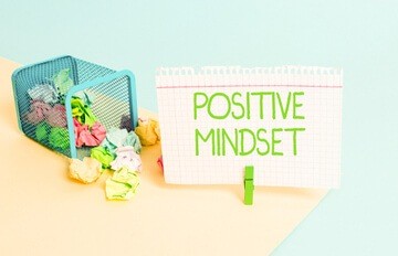a waste paper basket will colorful papers in it and in light green letters the statement Positive Mindset