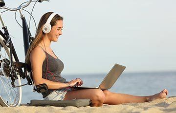 perfect setting: young woman leaning back on bicycle, at the seashore, with laptop, and high end earphones for music