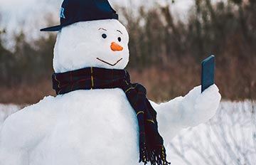 a snowman wearing a baseball cap and playing games on his cell phone