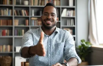 a smiling man extending his hand to shake another person's hand (not seen) as a gesture of reaching out to a customer or client