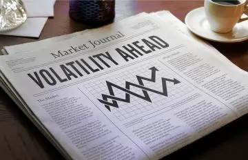 a newspaper, Market Journal, on a desk with the headline "volatility ahead". There is also a cup of black cofee on the desk.