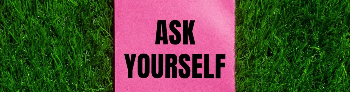 a sign on pink paper set against a green, synthetic grass background with black letters saying 