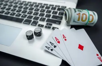 dice and cards sitting on a laptop with a roll of $100 bills