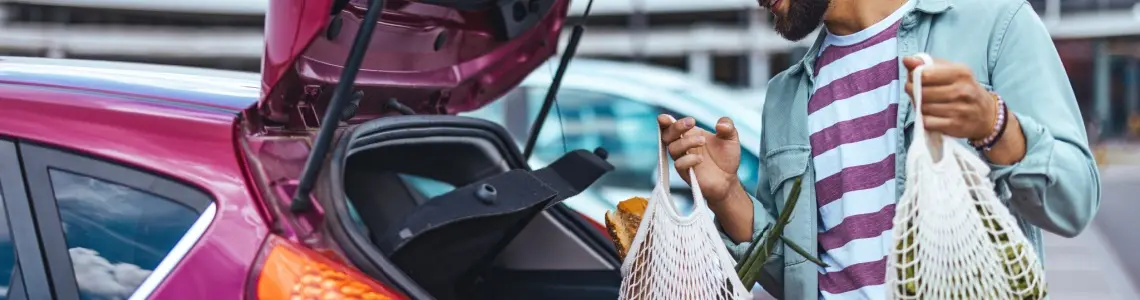 a man loading groceries into the trunk of his small, purple car. The car and easy shopping are examples of modern convenience.