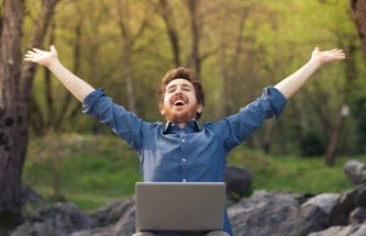 happy guy sitting in the forest with his laptop