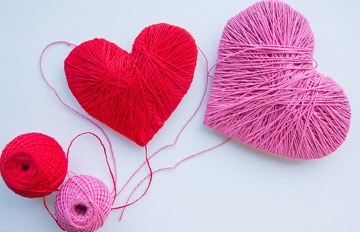 Two hearts, one red and one pink, that were created by a person using thread of those colors.