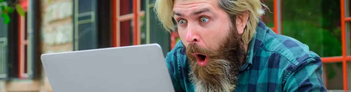 bearded young man with a happy, surprised expression while playing video poker on his laptop