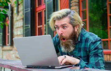 bearded young man with a happy, surprised expression while playing video poker on his laptop