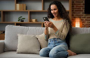 attractive young woman with long curly dark brown hair happily playing casino games on her mobile device lounging on the sofa