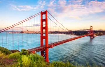 an arial view of the Golden Gate Bridge in San Francisco with blue water beneath it and hills in the background