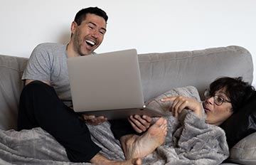happy couple playing online casino games on their sofa. He is barefoot and his wife in reclining on her back