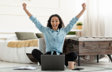 young woman sitting on the floor pumping her fists because she has won at an online casino game